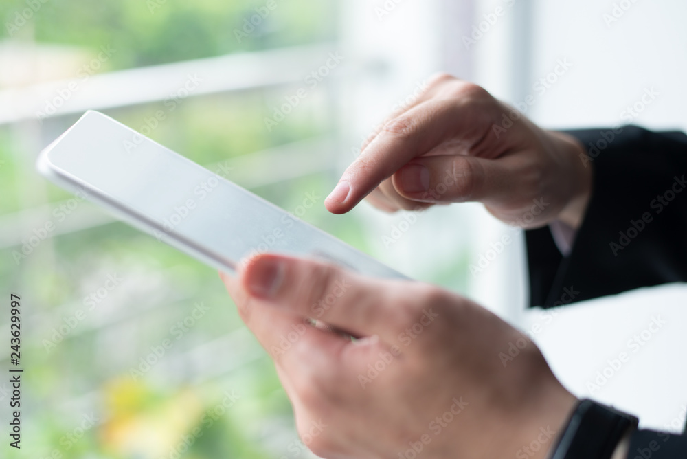 Closeup of business person using tablet at window. Man tapping on touchscreen with window and green view in background. Technology and communication concept. Cropped side view.