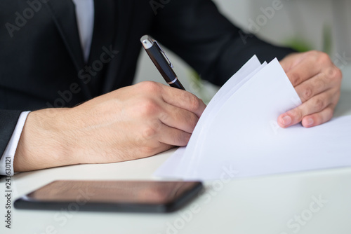 Closeup of entrepreneur signing document at office desk. Business man wearing suit and working. Contract concept. Cropped view.