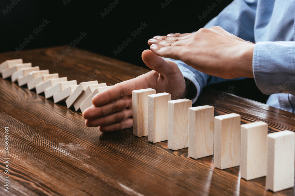 cropped view of woman sitting at desk and preventing wooden blocks from falling