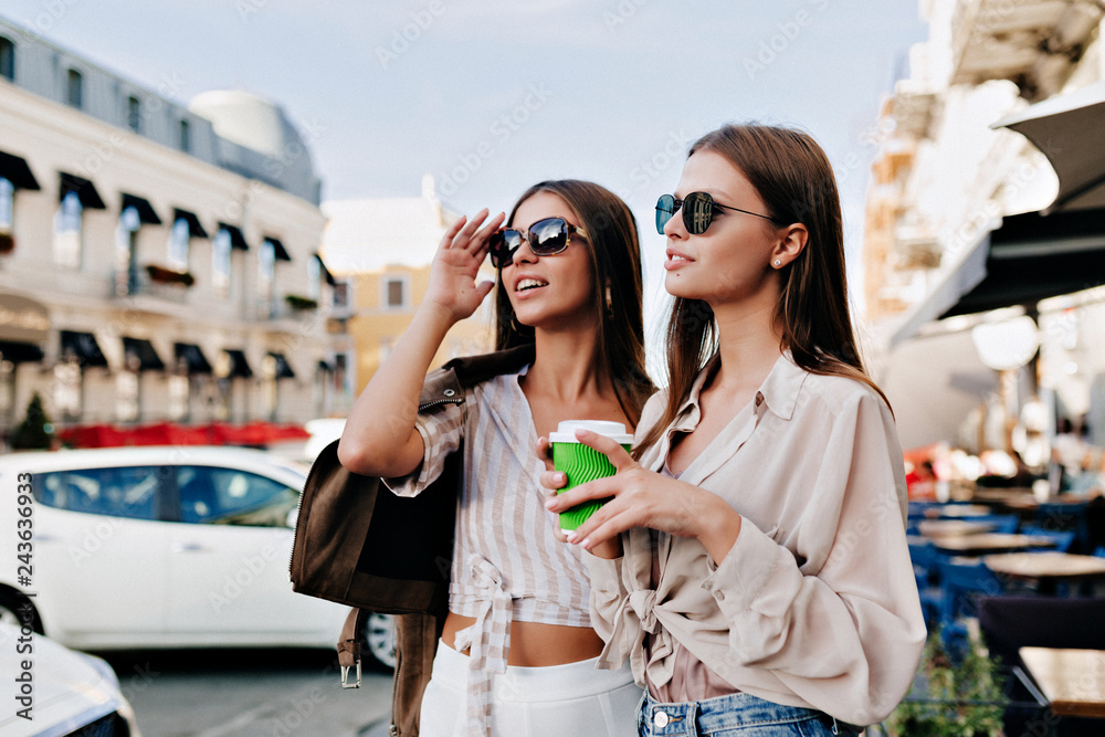 Charming laughing ladies posing together on city background. Outdoor photo of interested caucasian ladies enjoying good day.