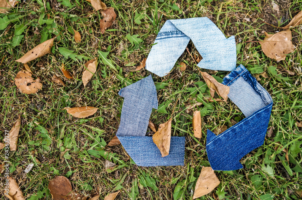 Fototapeta premium Recycle symbol made from textile over green grass background