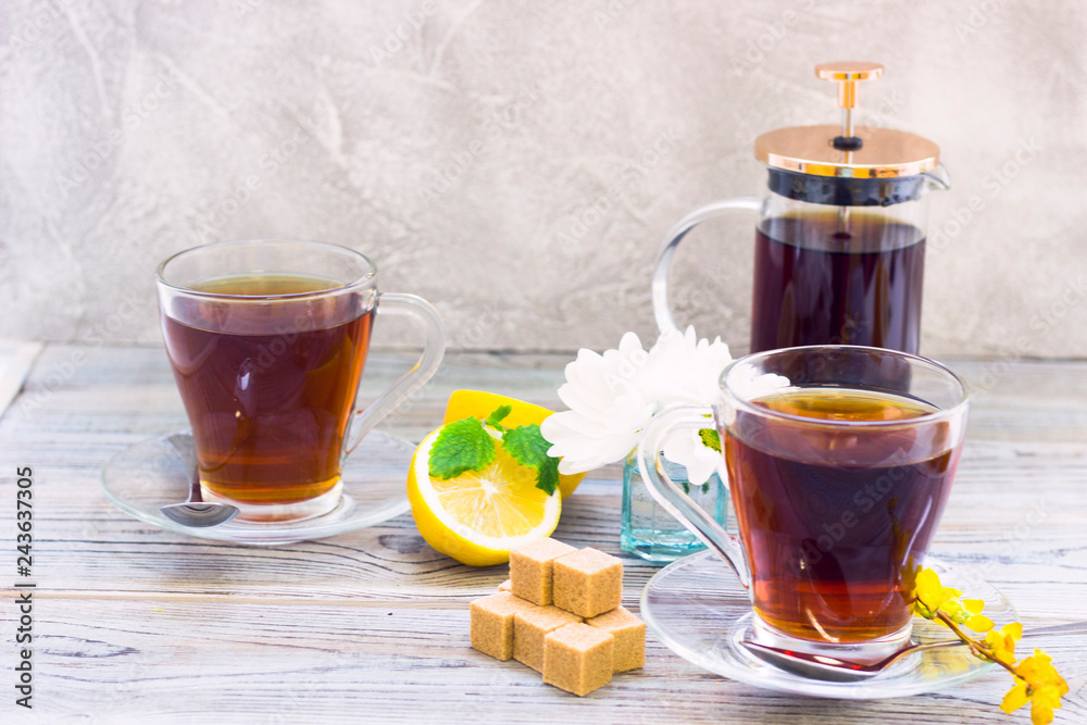 Black tea ceremony - glass full of tea, glass pot, sugar, yellow lemon, flower, tea leaves, spices on a wooden boards background Black tea ceremony - glass full of tea, glass pot, sugar, yellow lemon, flower, tea leaves, spices on a wooden boards background
