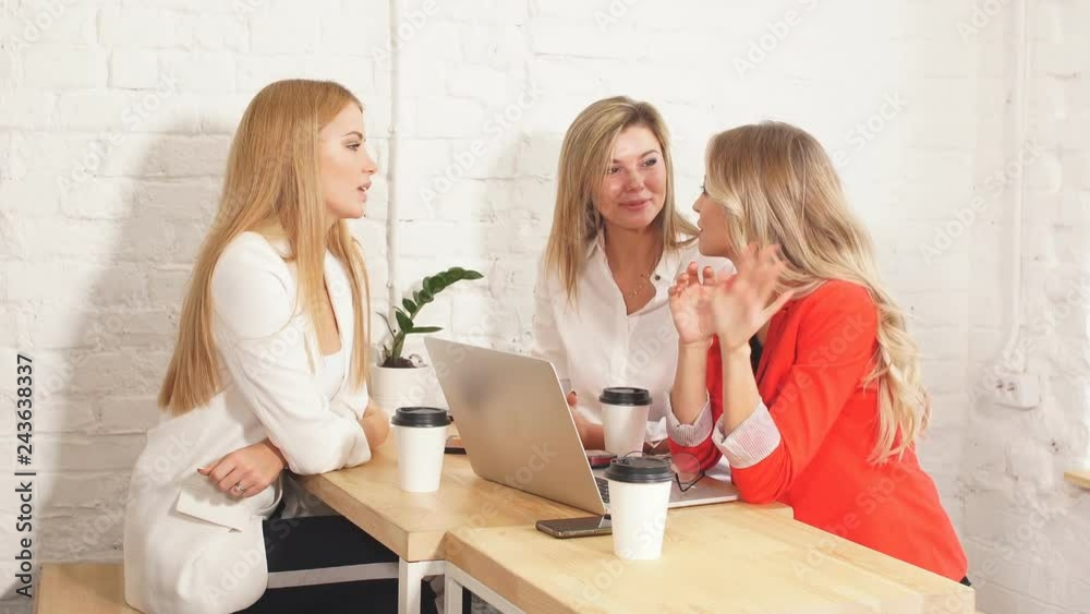 Group of young modern women in bright colourful casual wear discussing topics while sitting in the coffee shop Group of young modern women in bright colourful casual wear discussing topics while sitting in the coffee shop