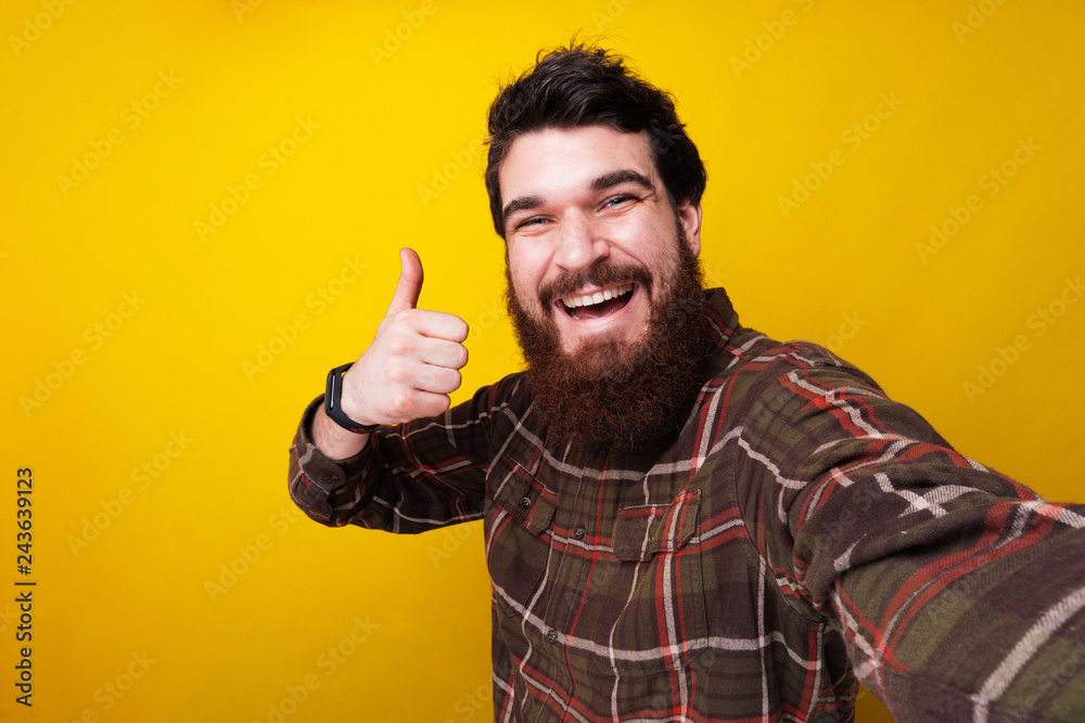 Amazed man with beard showing thumbs up over yellow background Amazed man with beard showing thumbs up over yellow background