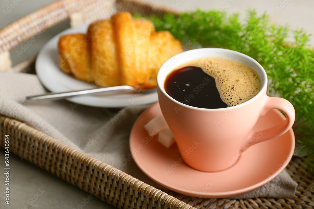 Cup of hot coffee and plate with croissant on tray