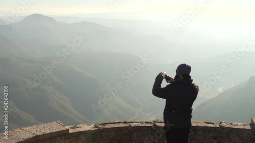 The guy on the observation deck looks at a beautiful view of the mountains in the haze and taking pictures photo