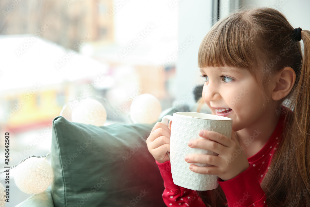 Cute little girl drinking hot chocolate near window