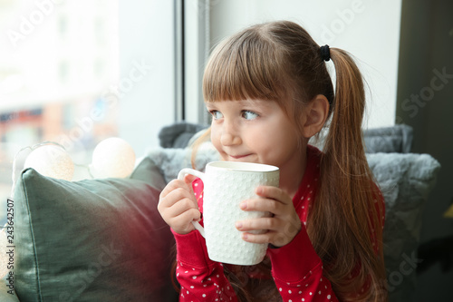 Cute little girl drinking hot chocolate near window