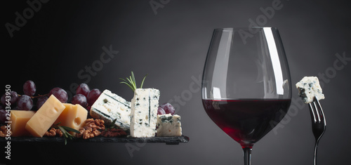 Glass of red wine with various cheeses, grapes, walnuts and rosemary.