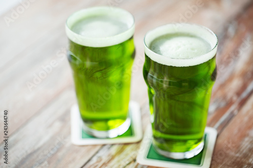 st patricks day, holidays and celebration concept - two glasses of green beer on wooden table