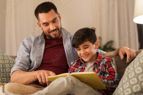 family, childhood, fatherhood, leisure and people concept - happy smiling father and little son reading book on sofa at home