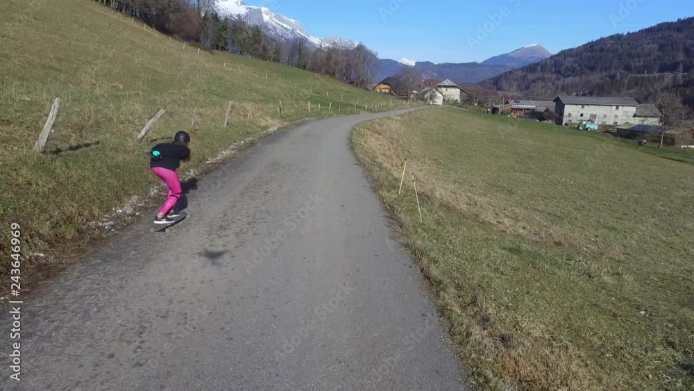 jeune fille de dos en skate longboard rouland vers un village de montagne filmé photographié par drone jeune fille de dos en skate longboard rouland vers un village de montagne filmé photographié par drone