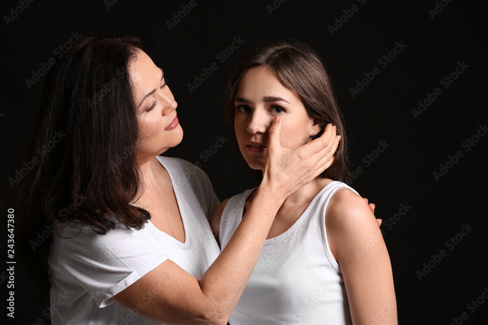 Woman calming her daughter on dark background Woman calming her daughter on dark background