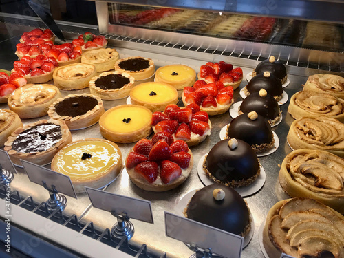 Obraz na plátně Pastry shop with variety of tarts, cakes, creme brulee, with strawberry, chocolate, lemon, pears and apple slices displayed at showcase