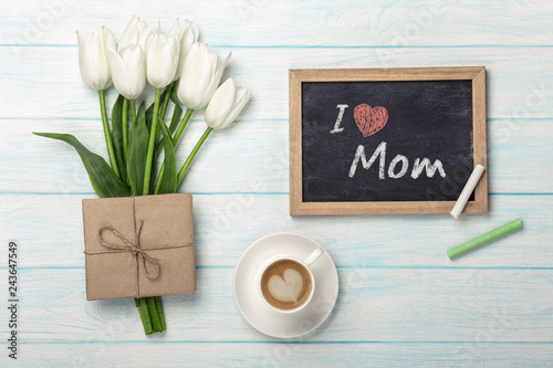 A bouquet of white tulips, cup of coffee with chalk board and envelope on blue wooden boards . Mother's day