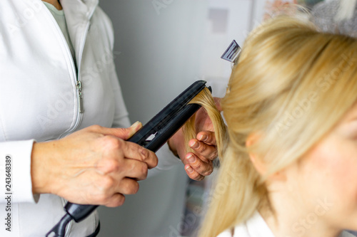 Hairdresser holding strand of girls blonde hair with flat iron making beautiful curls