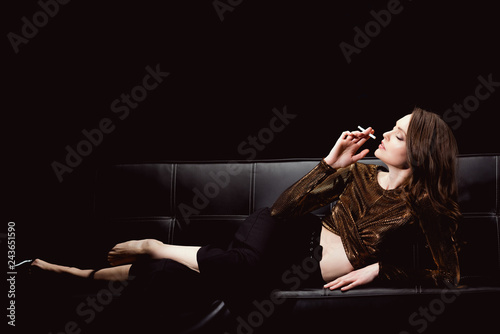 beautiful glamorous woman lying on couch and smoking cigarette isolated on black