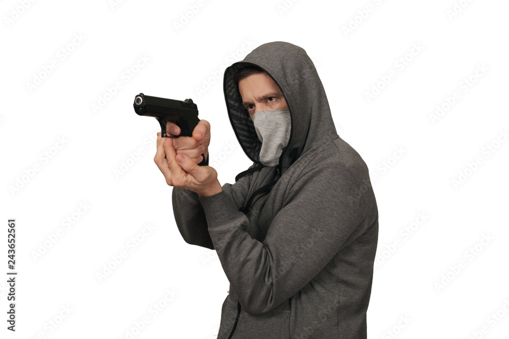 The man in a sports gray jacket and in a mask on a face shoots with the gun. White background The man in a sports gray jacket and in a mask on a face shoots with the gun. White background