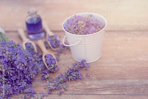 Fototapeta Naklejka Na Ścianę i Meble -  Top view of a bowl and wooden spoons with fresh lavender flowers, lavender essential oil and a bouquet of lavender on a brown wooden background.