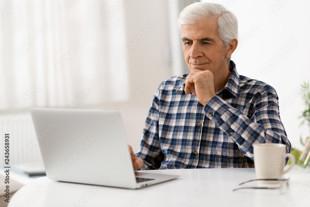 Happy mature man relaxing at home and using laptop Happy mature man relaxing at home and using laptop