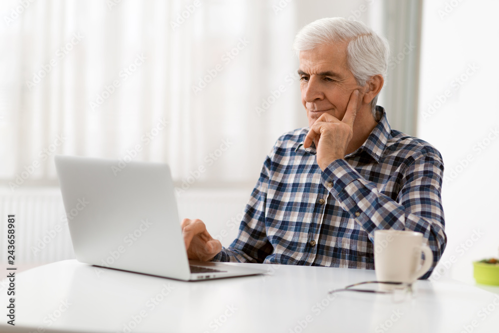 Happy mature man relaxing at home and using laptop Happy mature man relaxing at home and using laptop