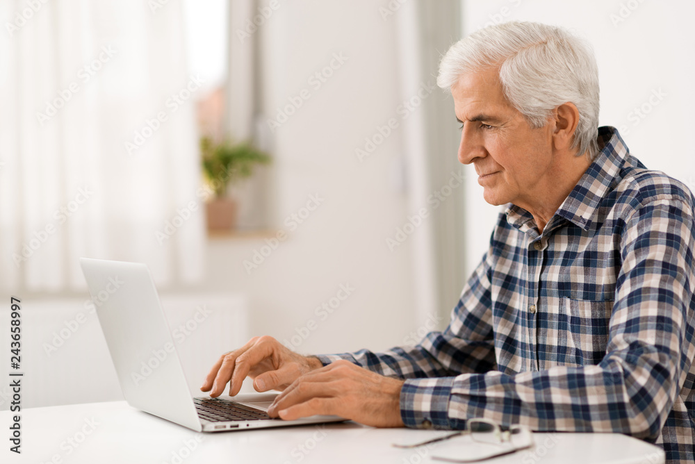 Serious mature man relaxing at home and using laptop Serious mature man relaxing at home and using laptop