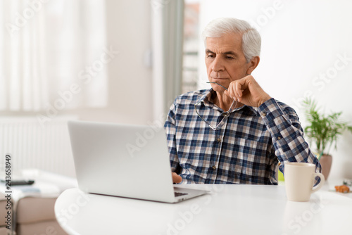 Senior man surfing the internet on laptop in the living room