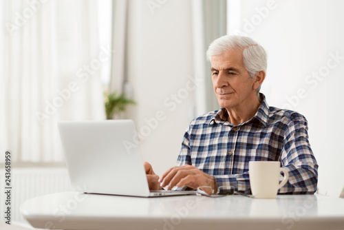 Happy mature man relaxing at home and using laptop