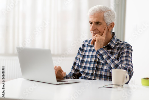 Happy mature man relaxing at home and using laptop