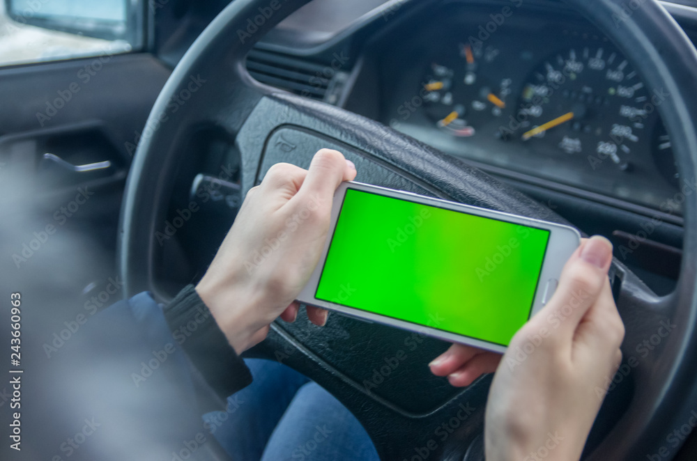 The girl is holding a white phone with a green screen above the wheel of a car
