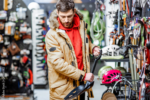 Man in winter jacket choosing mountaineer equipment holding snow shovel in the sports shop