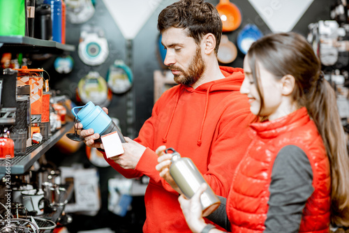 Young couple dressed in red sportswear choosing dishes for camping in the shop with travel equipment