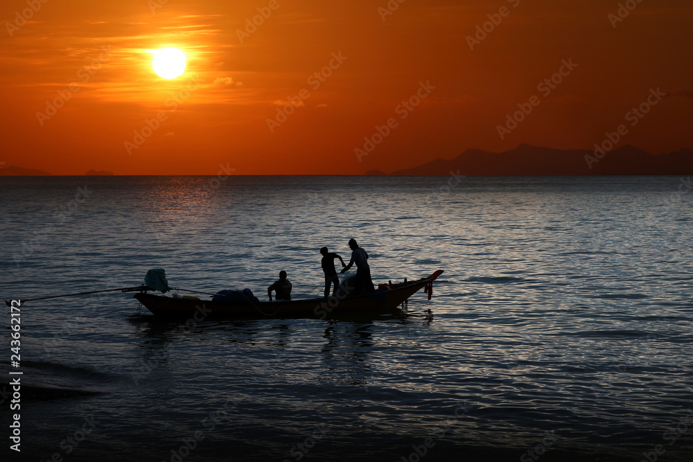 Local fishermen on a long-tail boat in the sea at sunset