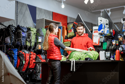 Fototapeta Naklejka Na Ścianę i Meble -  Young woman buying some sports goods standing with salesman at the counter of the shop