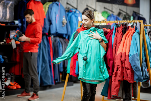 Young woman choosing winter clothes trying windbreaking jacket in the sports shop