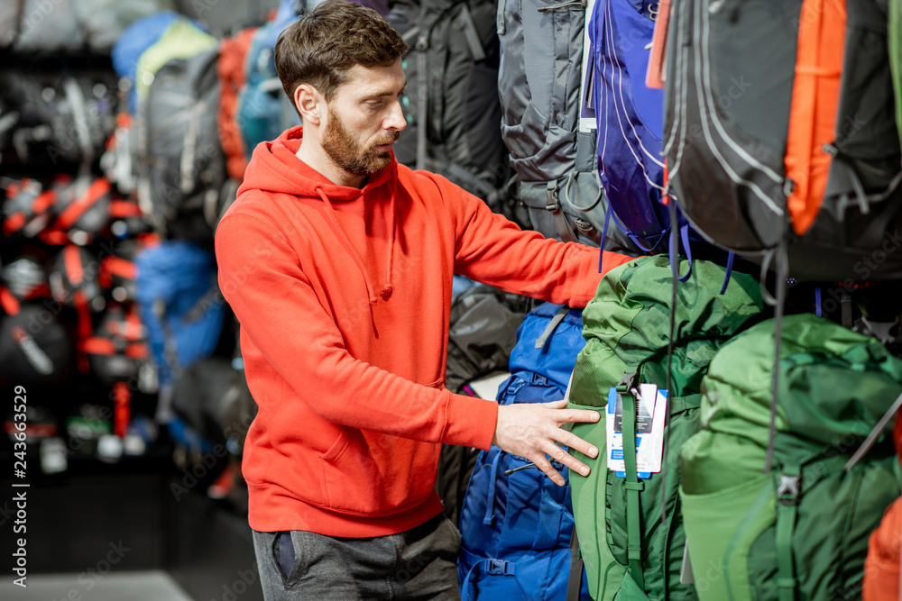 Man choosing some sports equipment looking on the backpacks for traveling in the sports shop Man choosing some sports equipment looking on the backpacks for traveling in the sports shop