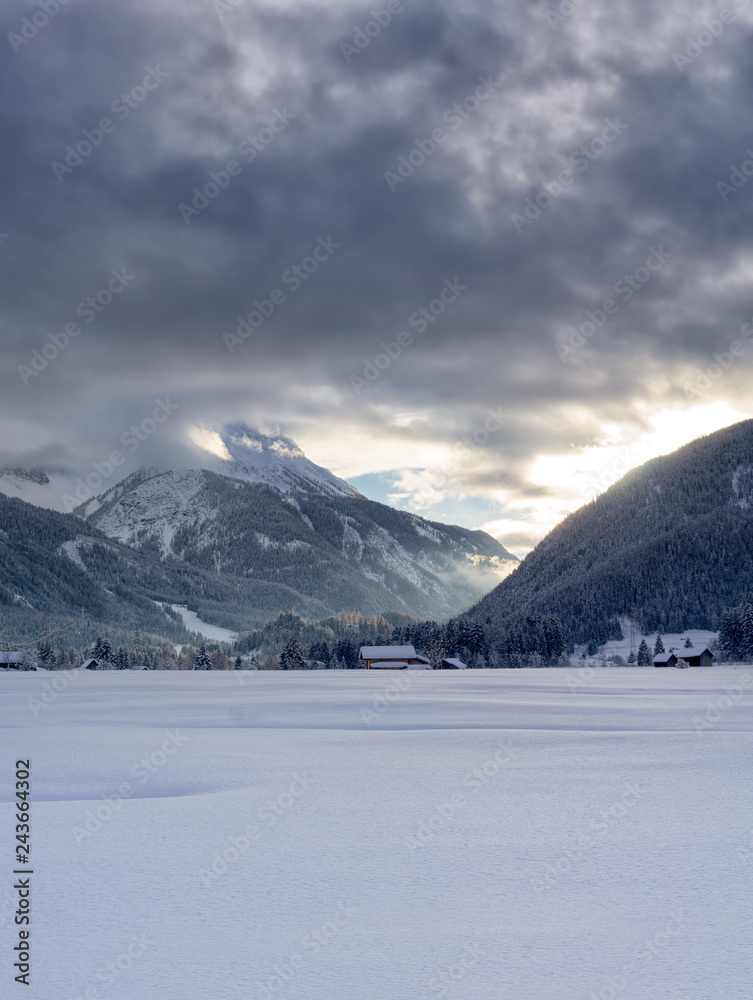 Winter mountain landscape at dusk. The setting sun illuminates dark clouds. Fog is falling in the valley.