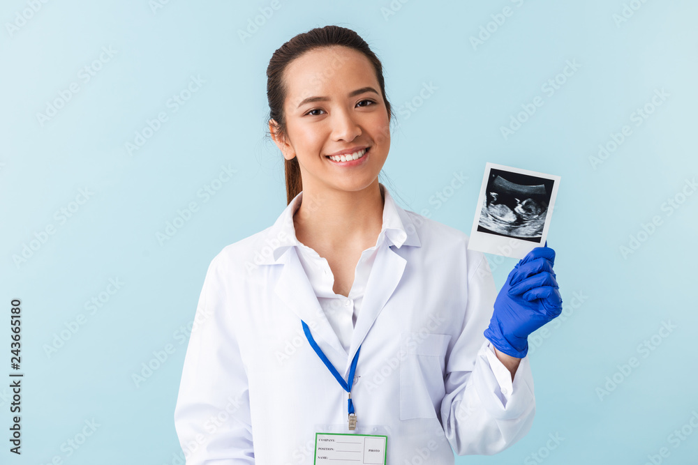 Woman doctor posing isolated over blue wall background holding x-ray of baby in hands. Woman doctor posing isolated over blue wall background holding x-ray of baby in hands.