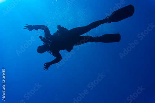 Diver underwater in deep blue sea. Man in diving gear dives up to water surface. Open water diving lesson. Beautiful ocean with sun rays in water. Diver man silhouette undersea photo. Seawater view