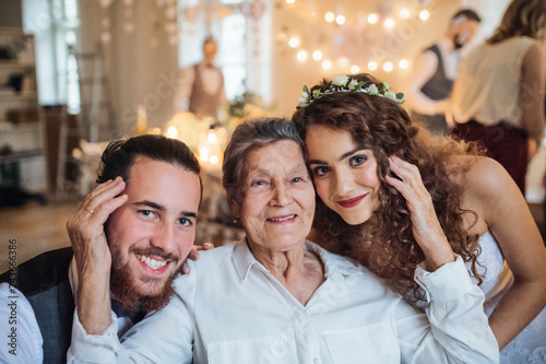 A young couple with grandmother on a wedding, looking at camera.