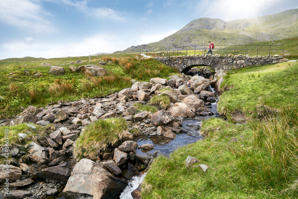 A hiker crossing Torver Bridge near Coniston on a sunny summers day in the English Lake District.