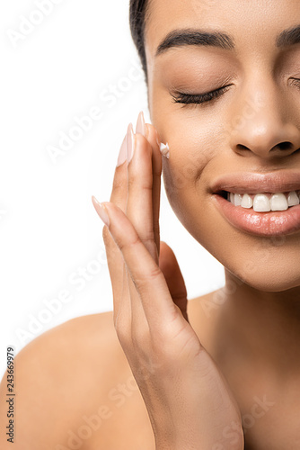 close-up view of happy young african american woman applying face cream isolated on white