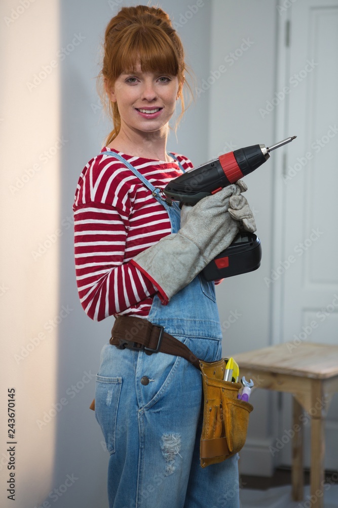 Female carpenter holding drill machine at home