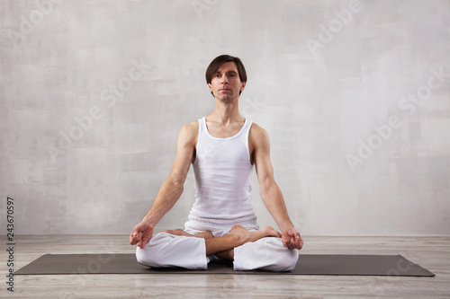 Young man in white clothes doing yoga in living room