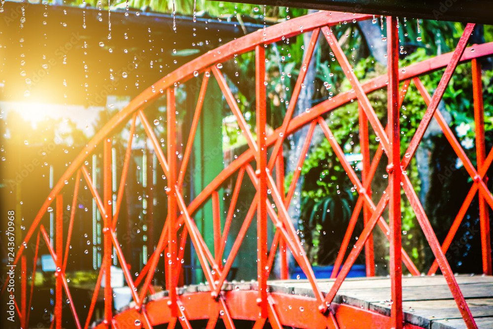 The red iron bridge is located in the falling rain and the sun shines through.