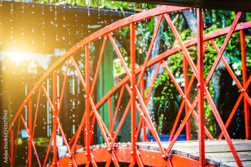 The red iron bridge is located in the falling rain and the sun shines through. © ronnakon