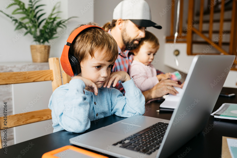 Father working at home, using laptop with his children on his lap Father working at home, using laptop with his children on his lap