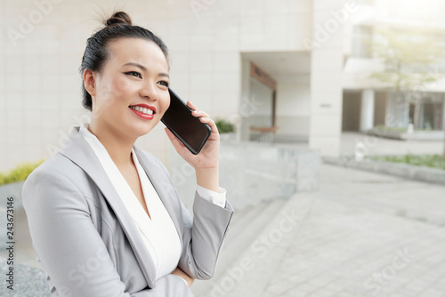 Positive smiling Asian business lady enjoying conversation on phone