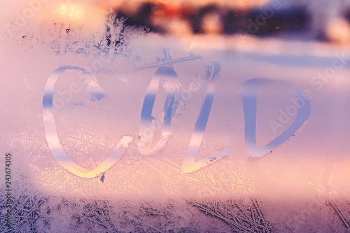 Word Cold on the frozen window glass. Hand written on the winter window