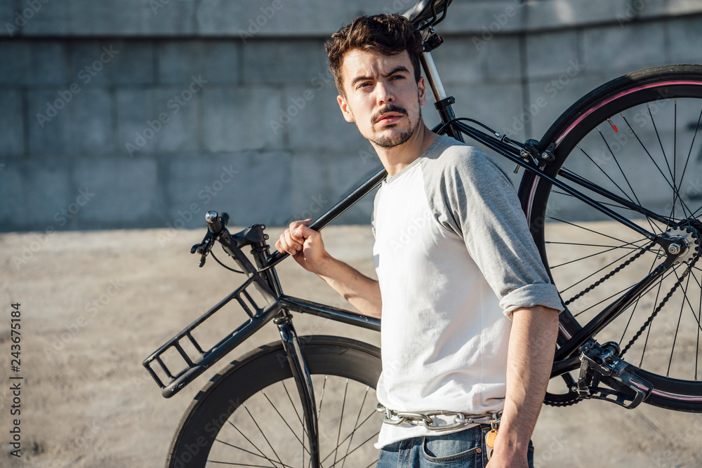 Young man carrying commuter fixie bike at concrete wall Young man carrying commuter fixie bike at concrete wall